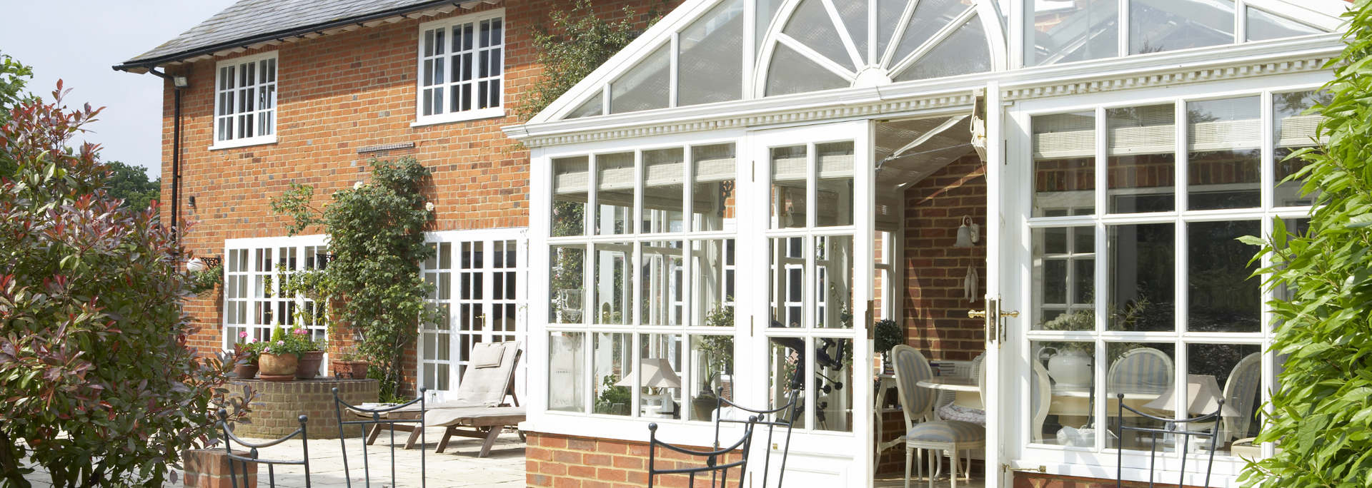 Brick house with a white glass conservatory and patio furniture in the garden