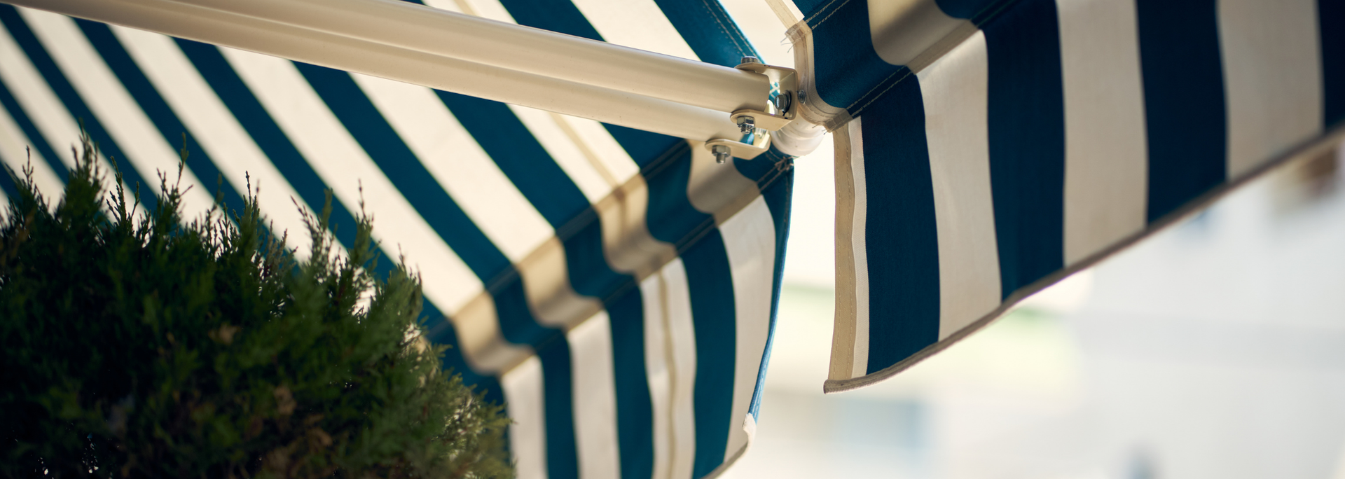 Blue-and-white striped awning over greenery against a bright sky