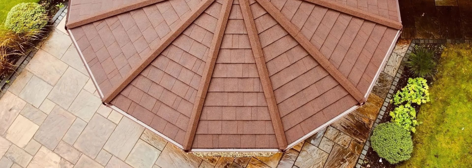 Aerial view of a brown octagonal gazebo roof surrounded by stone paving and shrubs