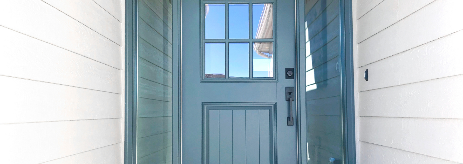 Light blue front door with window panes in white siding exterior wall