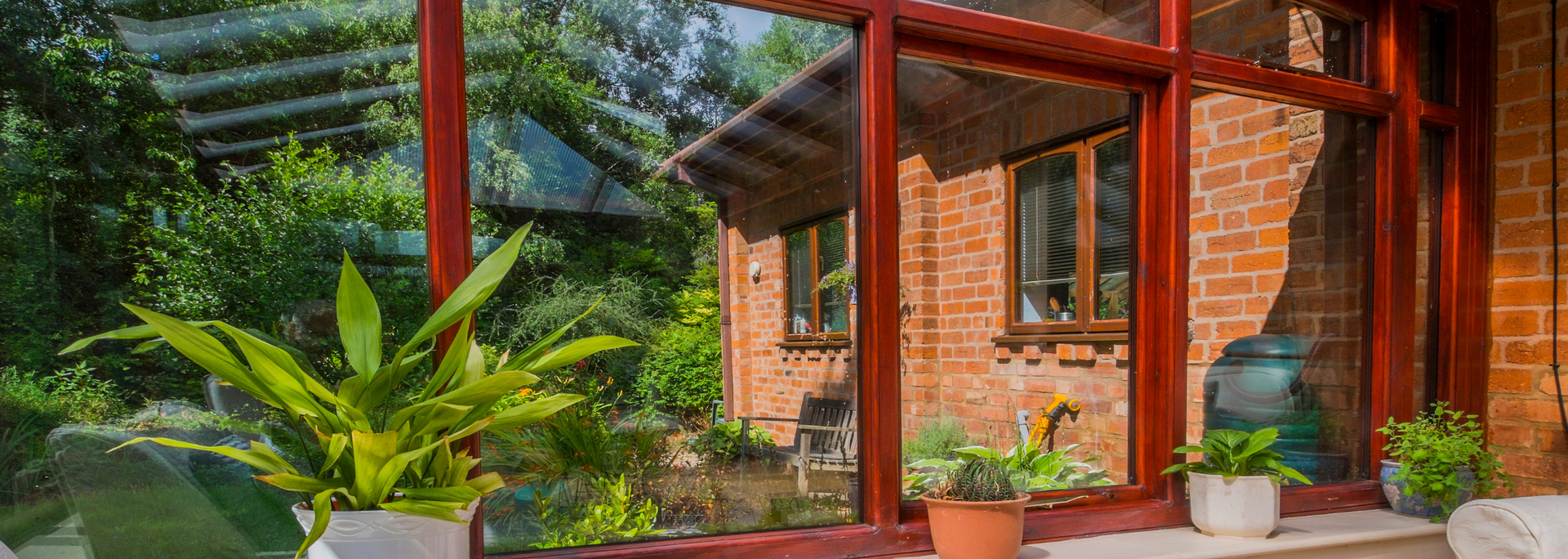 Brick house patio with red wooden beams, potted plants, and lush garden greenery