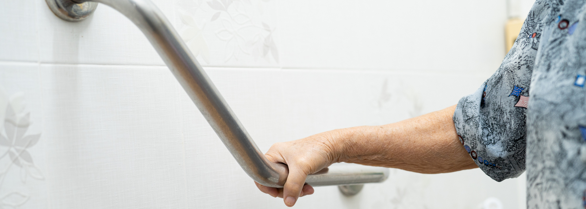 Hand gripping a metal grab bar in a white shower or bathroom stall