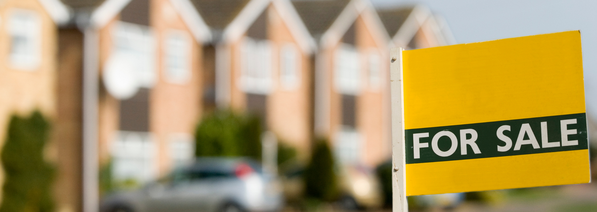 Yellow “For Sale” sign in front of blurred houses