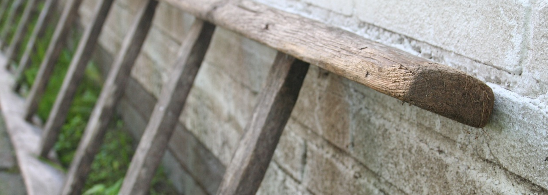 Rusty handrail along a slanted concrete wall beside green grass.