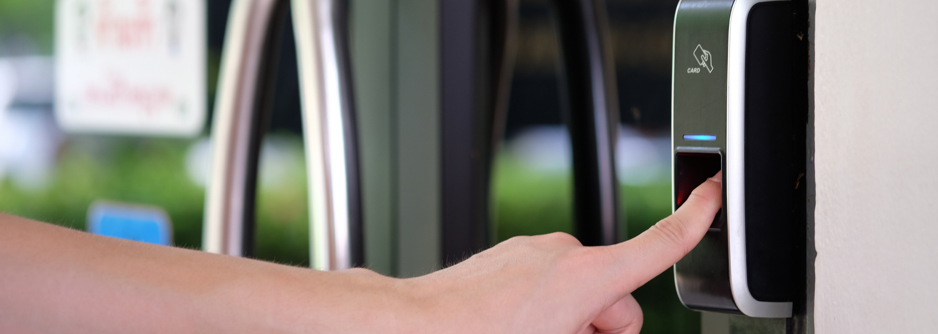 Hand pressing a key on a black biometric access panel beside a white door
