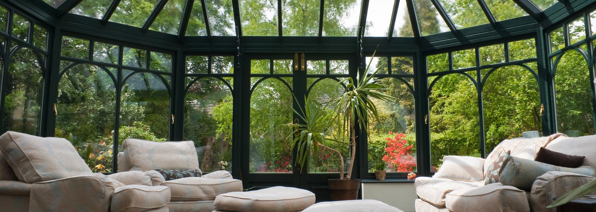 Sunlit conservatory with beige sofas and chairs around lush green garden views
