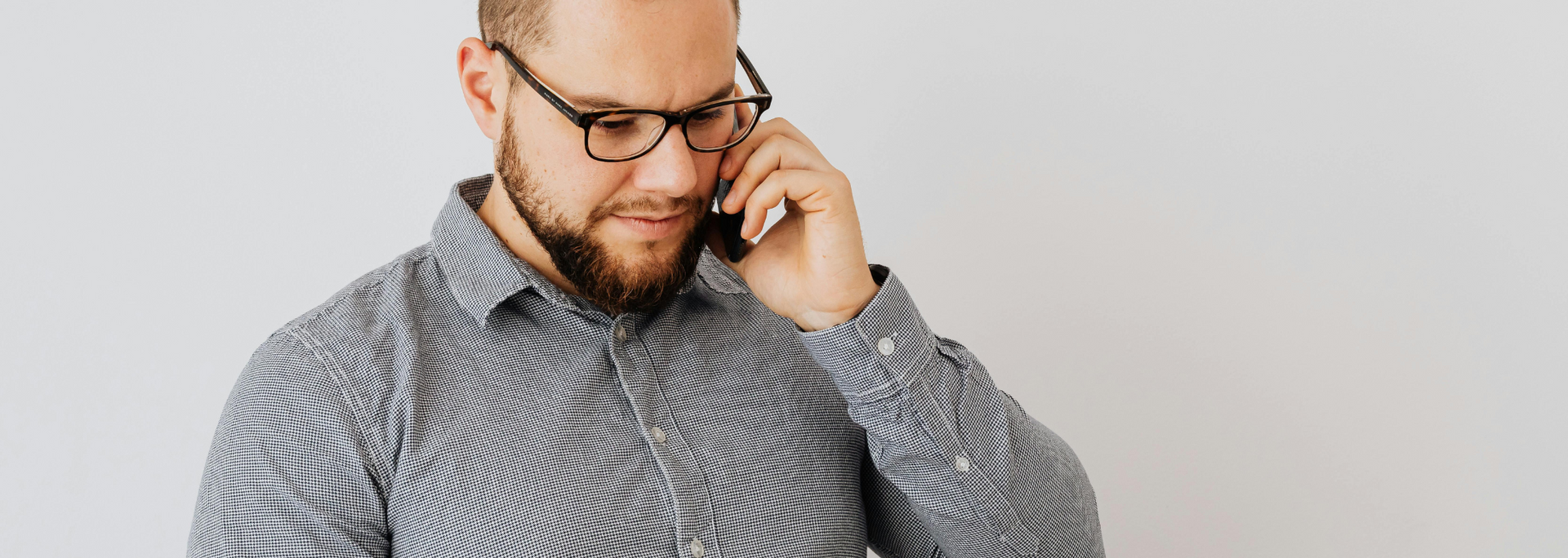 Man in glasses using a smartphone against a light gray background