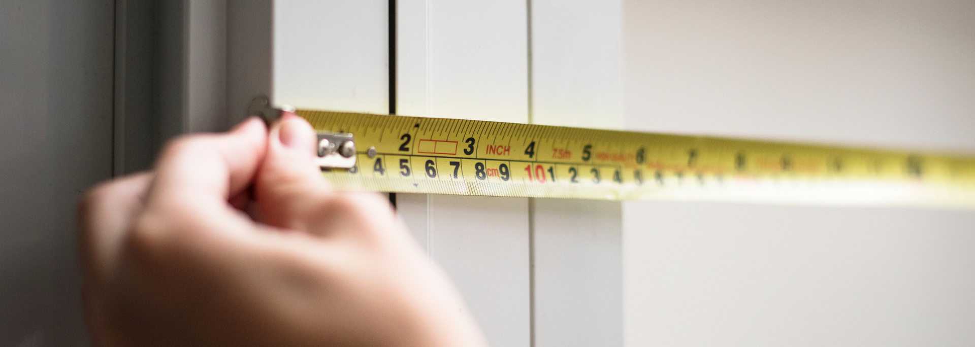 Hand holding a yellow tape measure across a white wall or door frame