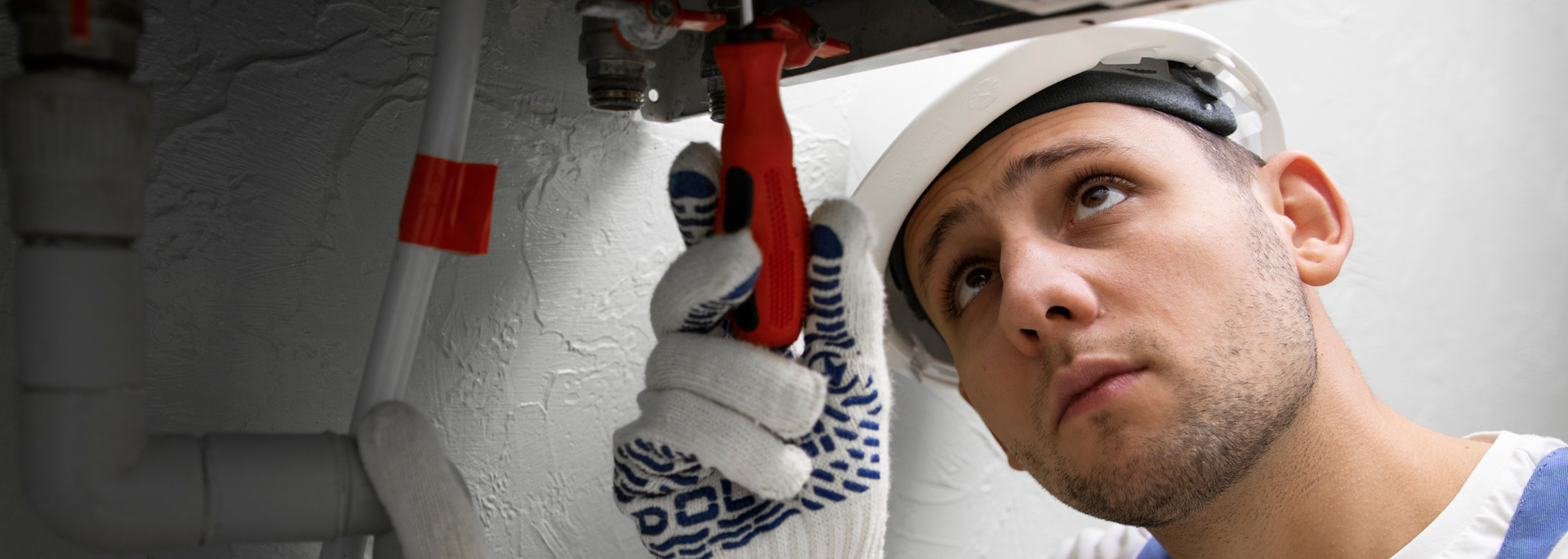 Worker in white gloves and hard hat inspecting pipes with a wrench indoors
