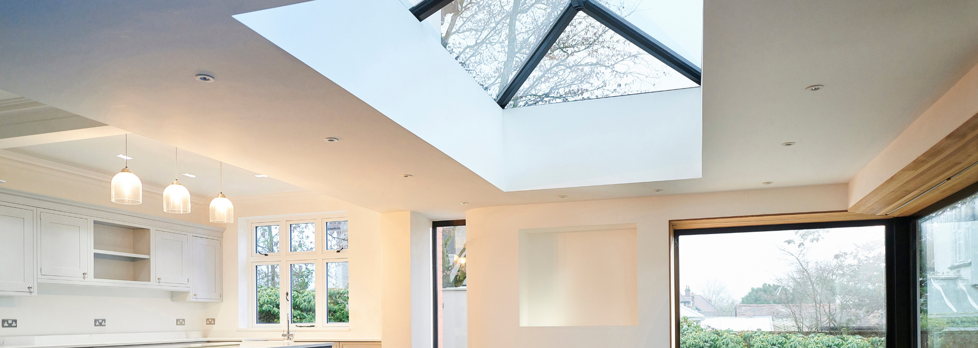 Bright modern kitchen and living room with skylight, white cabinetry, and large windows overlooking greenery