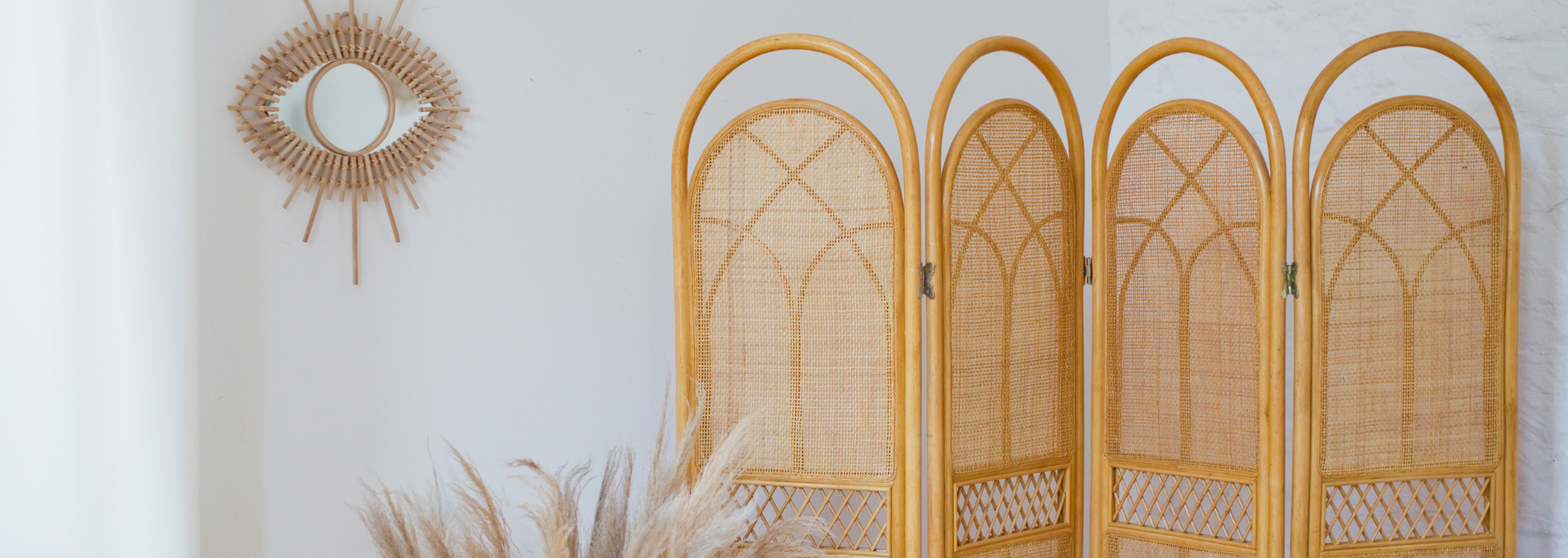 Boho wall decor with a gold sunburst mirror, woven screens, and dried grasses in a white room