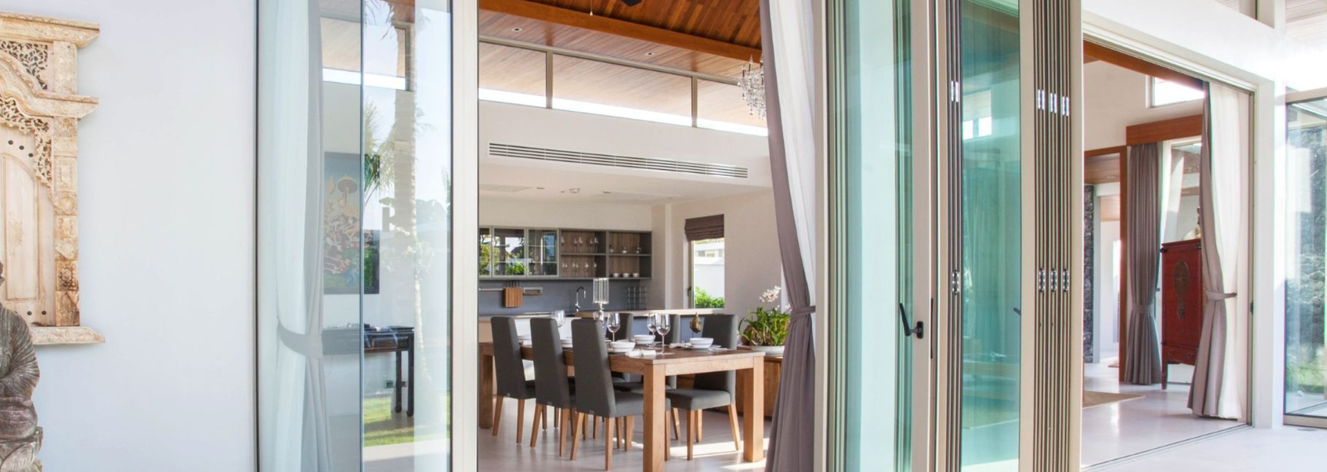 Open sliding glass doors to a bright dining room with wooden table and chairs, white walls, and exposed beams