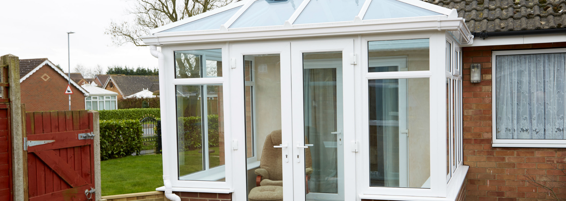 White conservatory with glass doors attached to a brick house in a garden