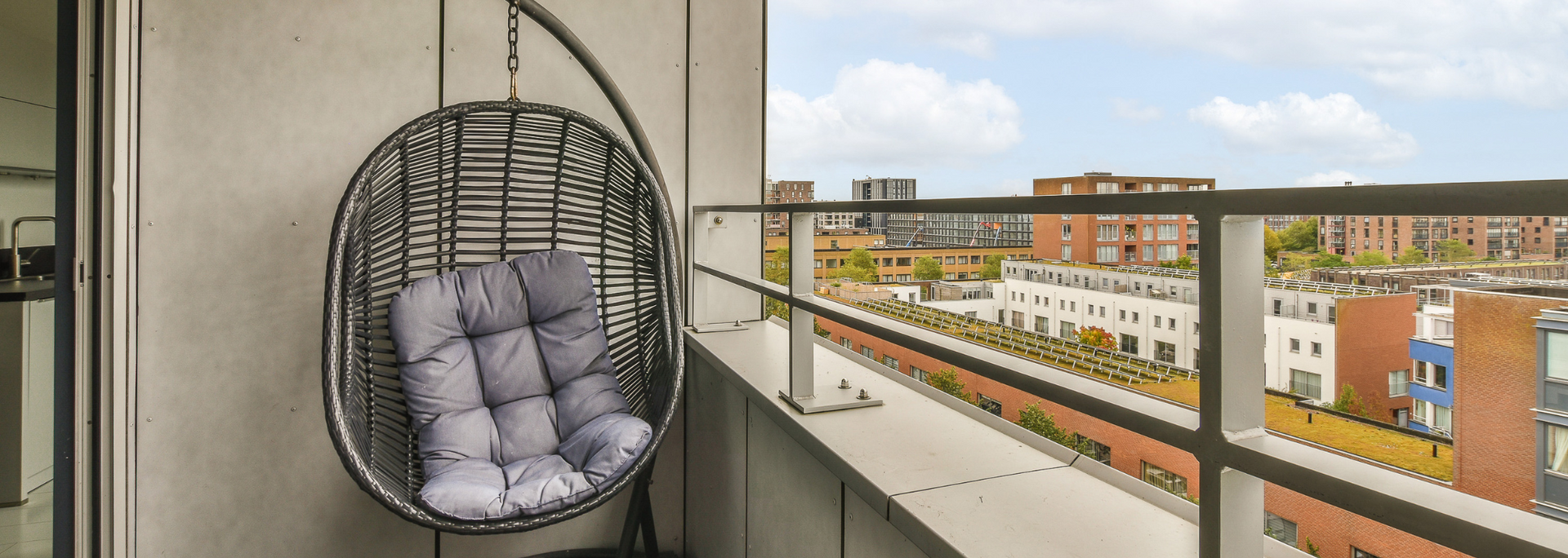 Hanging egg chair with gray cushion on a balcony overlooking apartment buildings