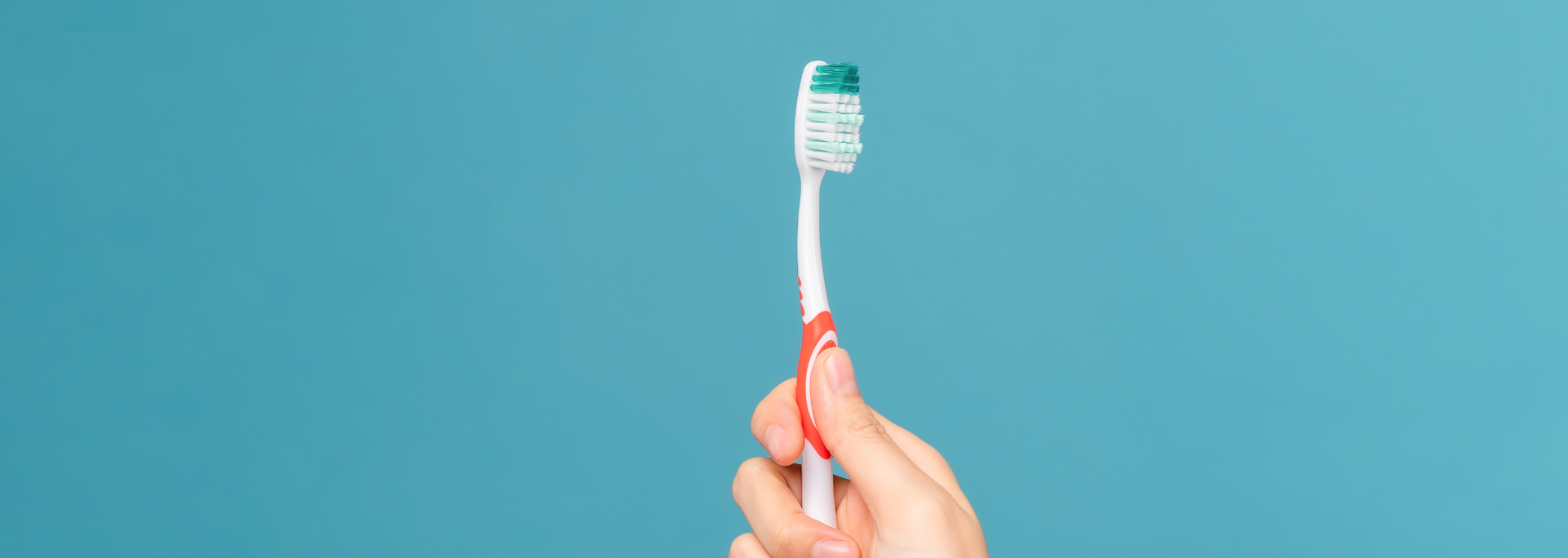 Hand holding a toothbrush with green toothpaste on a blue background