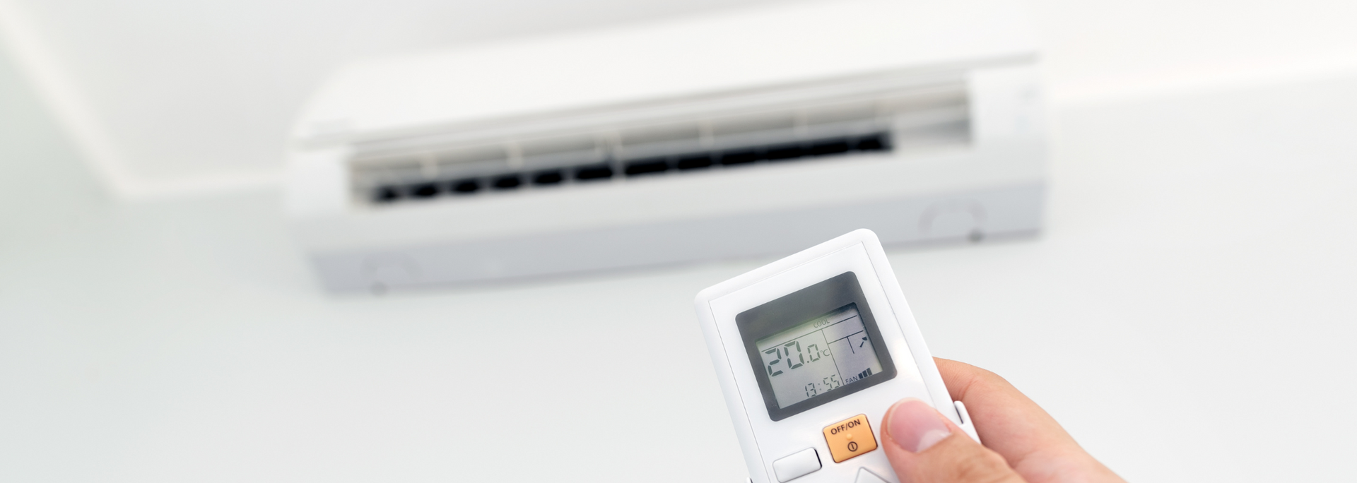 Hand holding a remote pointed at a wall-mounted air conditioner, adjusting the temperature