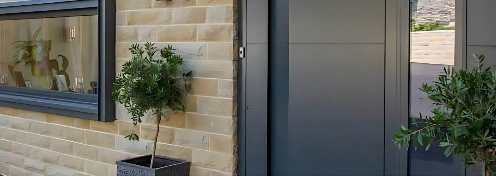 Modern building entrance with dark doors, beige brick walls, and potted plants on either side
