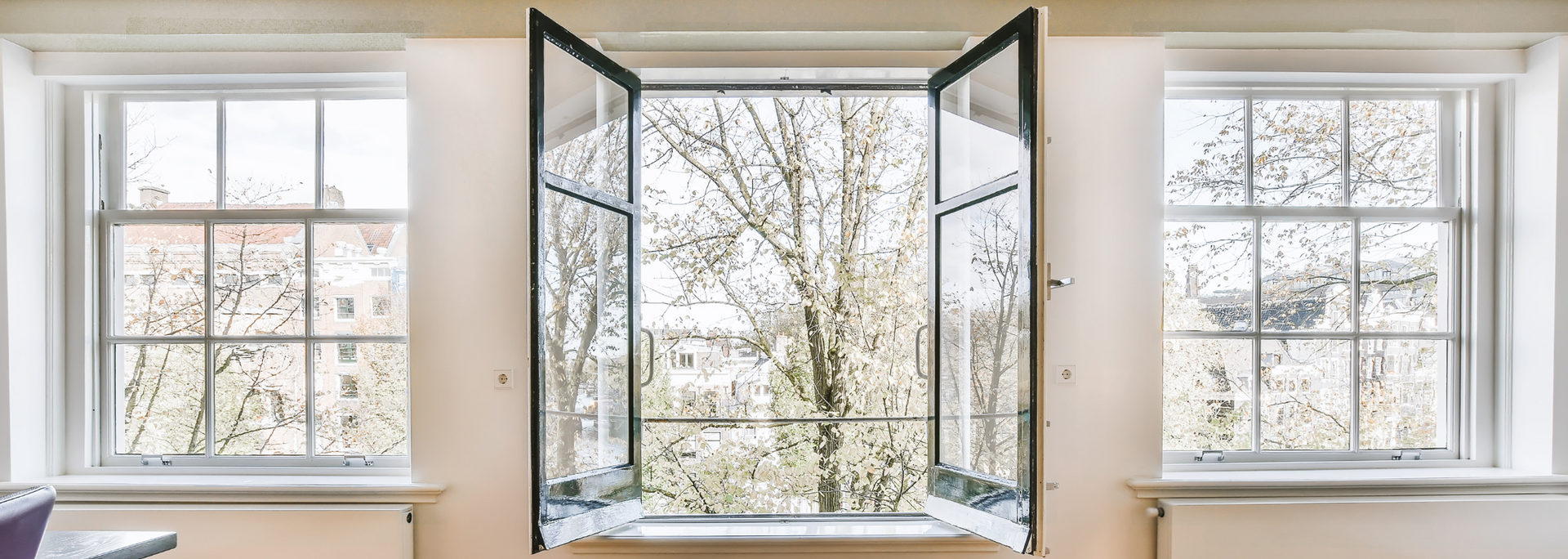 Open black-framed windows in a bright room, revealing trees outside.