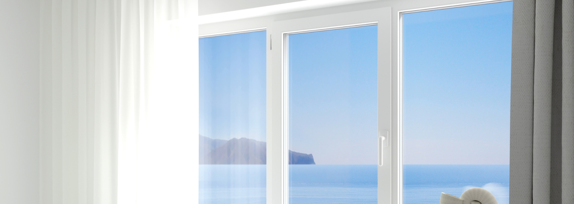 Bright window with white curtains overlooking a calm blue sea and distant island.