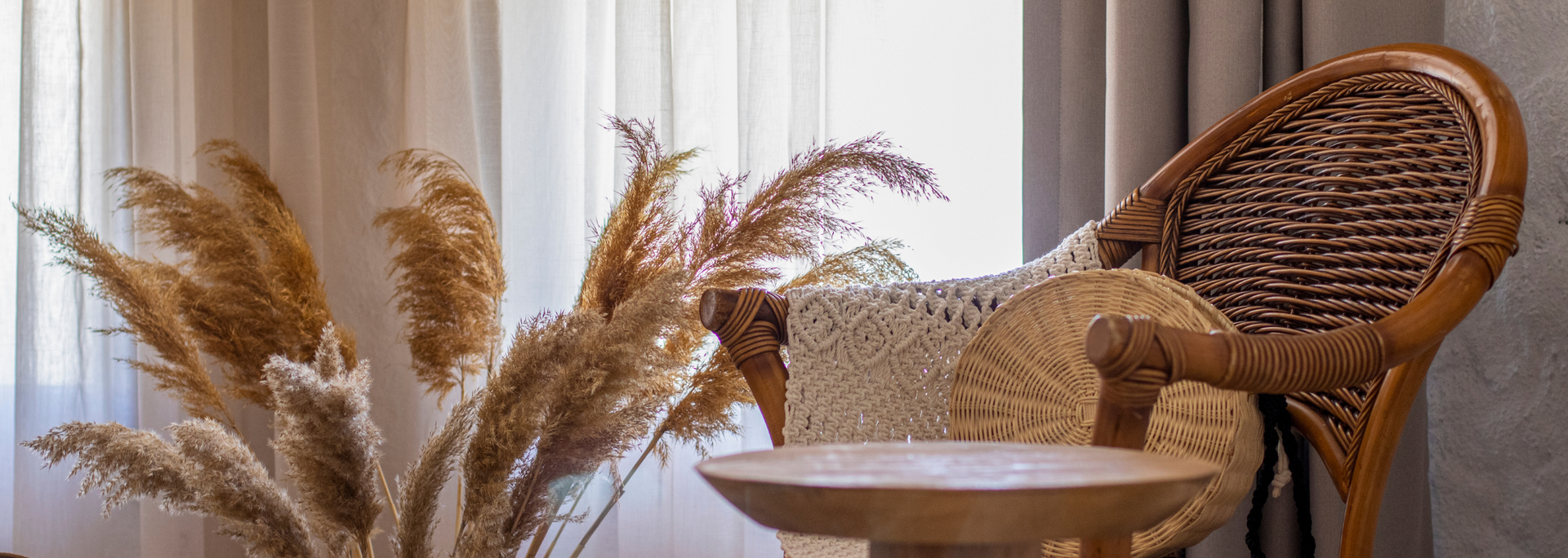 Wicker chair beside a small table with dried pampas grass in a bright, minimalist room