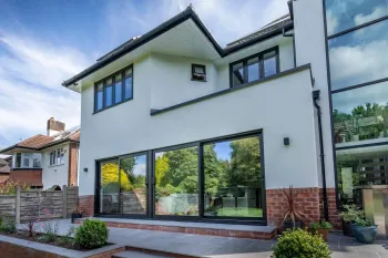 Modern white two-story house with black-framed windows, large glass doors, and red brick accents