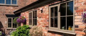 Brick house exterior with beige-framed windows and a flowering hanging basket in sunlight