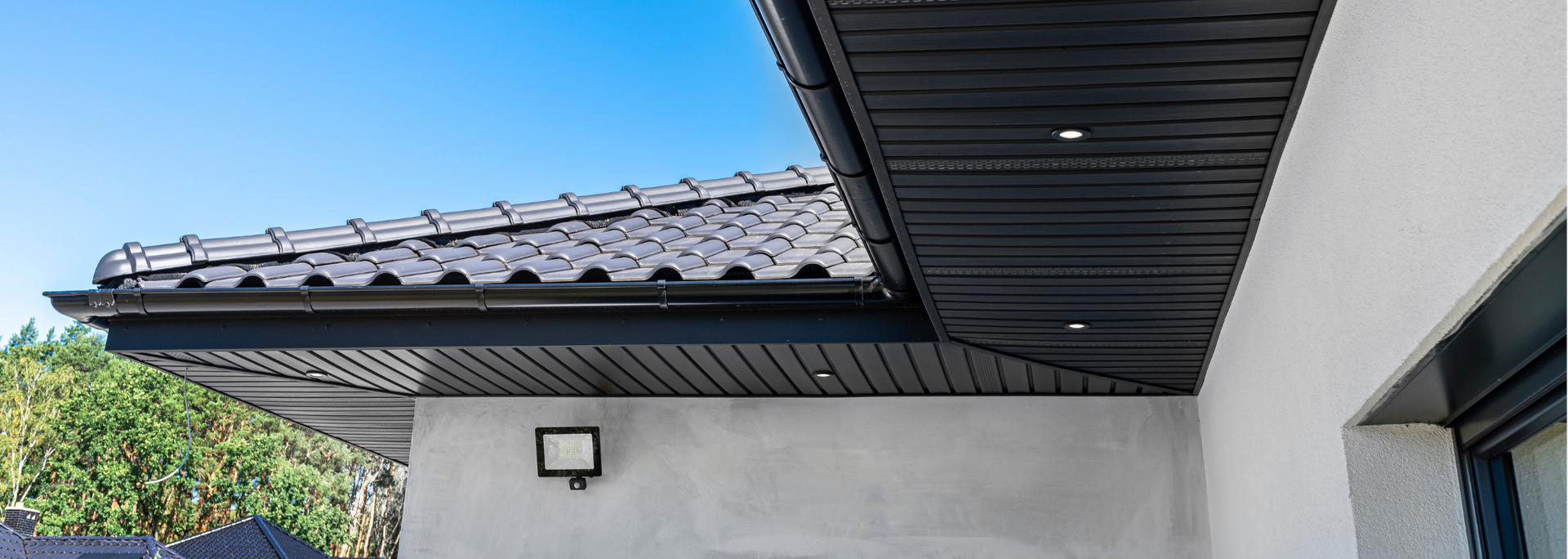 Exterior view of a house roof with dark gutters and white walls under a bright sky