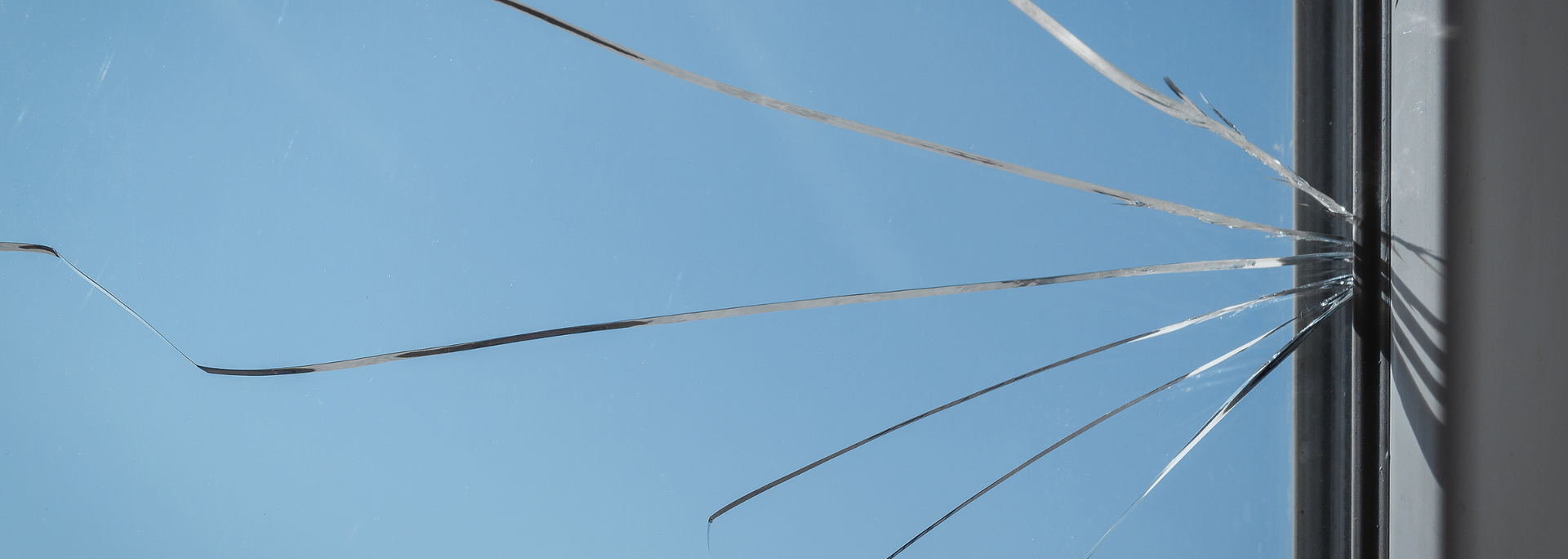 Cracked glass window with spiderweb fractures against a blue sky