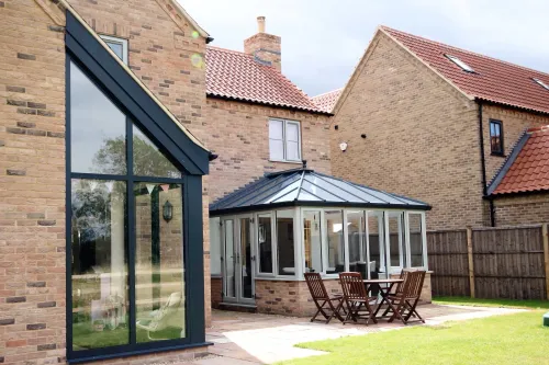 Backyard patio with glass conservatory, outdoor dining set, brick house, and lawn