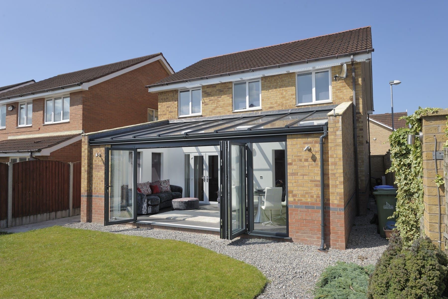Back garden with a glass conservatory attached to a brick house and a lawn in front