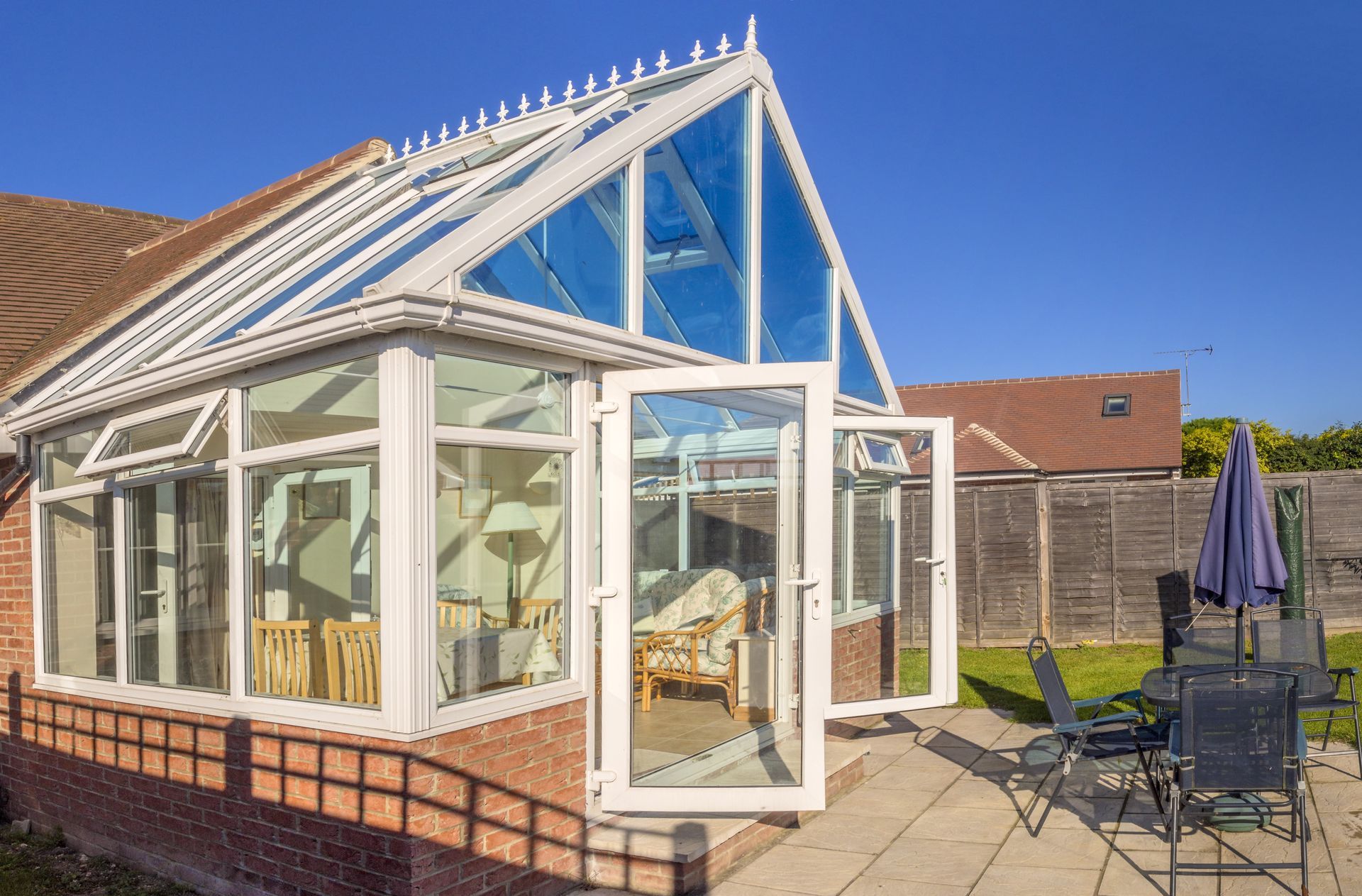 White glass conservatory with open door and patio furniture in a sunny backyard