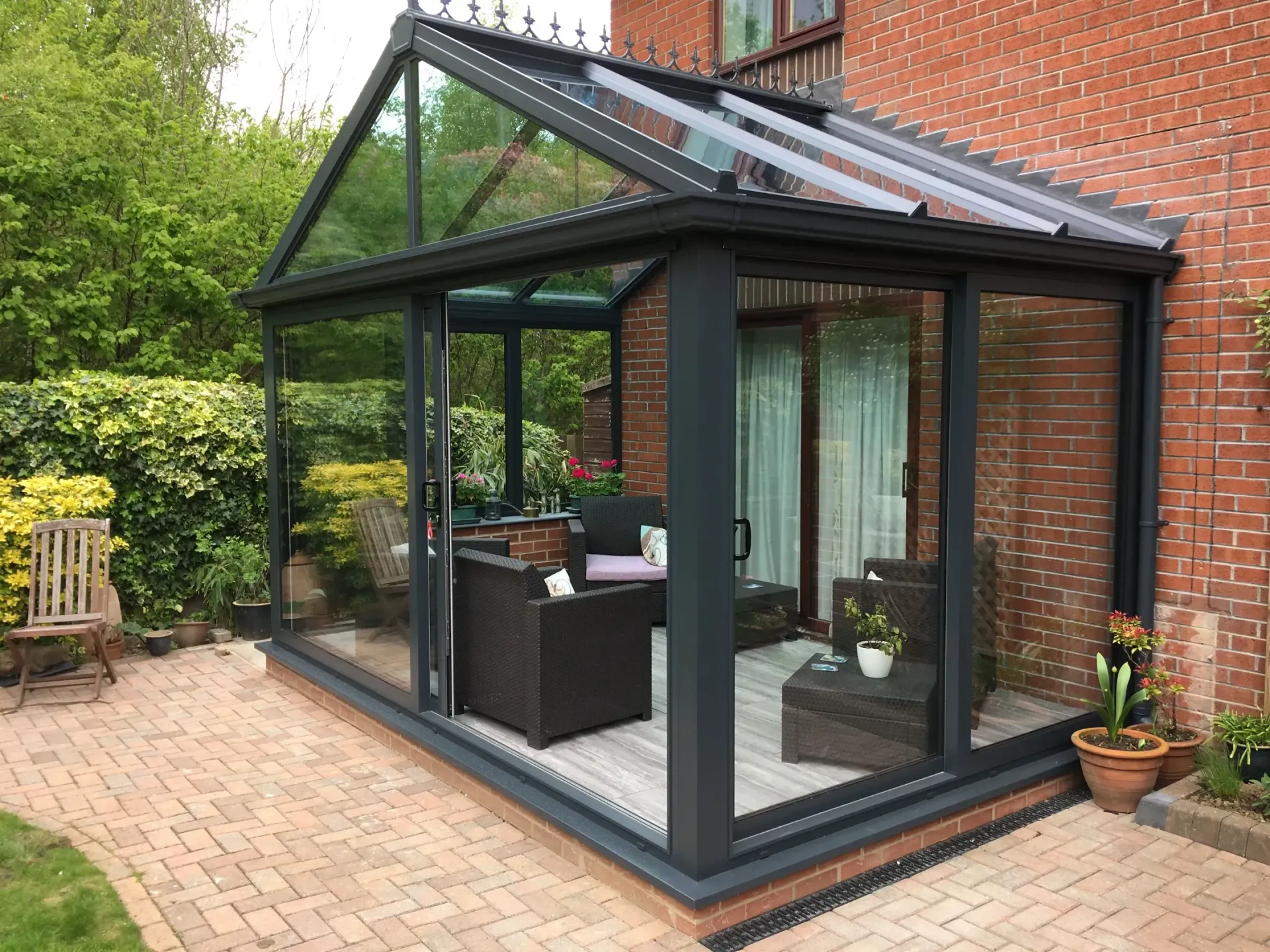 Glass sunroom conservatory attached to a brick house with wicker seating on a patio