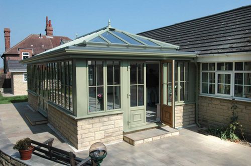 Glass conservatory attached to a brick house with a pale green door and windows.