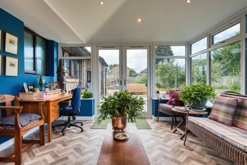 White conservatory extension attached to a brick house with a glass roof and windows