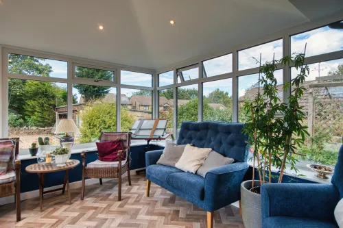 White conservatory extension attached to a brick house with a glass roof and windows