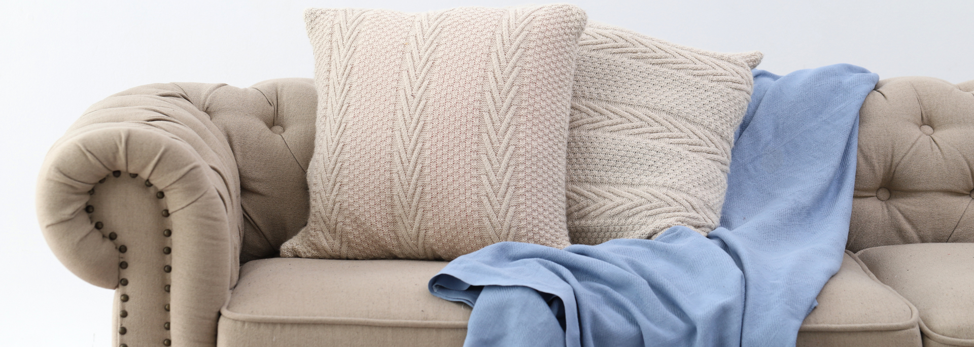 Beige sofa with cream pillows and a blue throw blanket draped across it