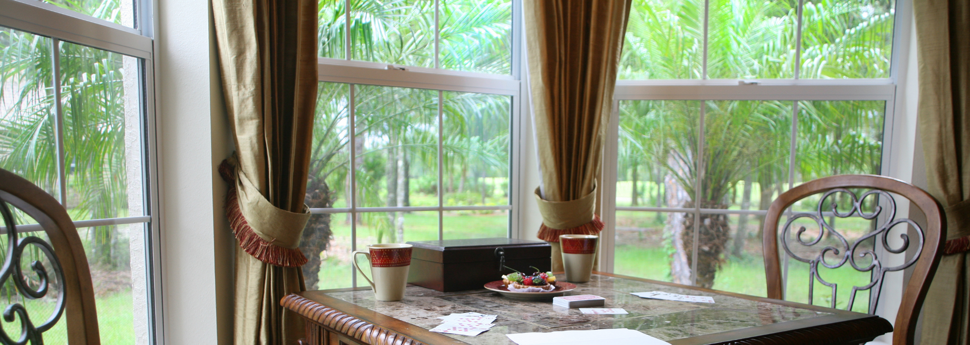 Sunlit dining table by large window with green garden view, curtains, and a chair