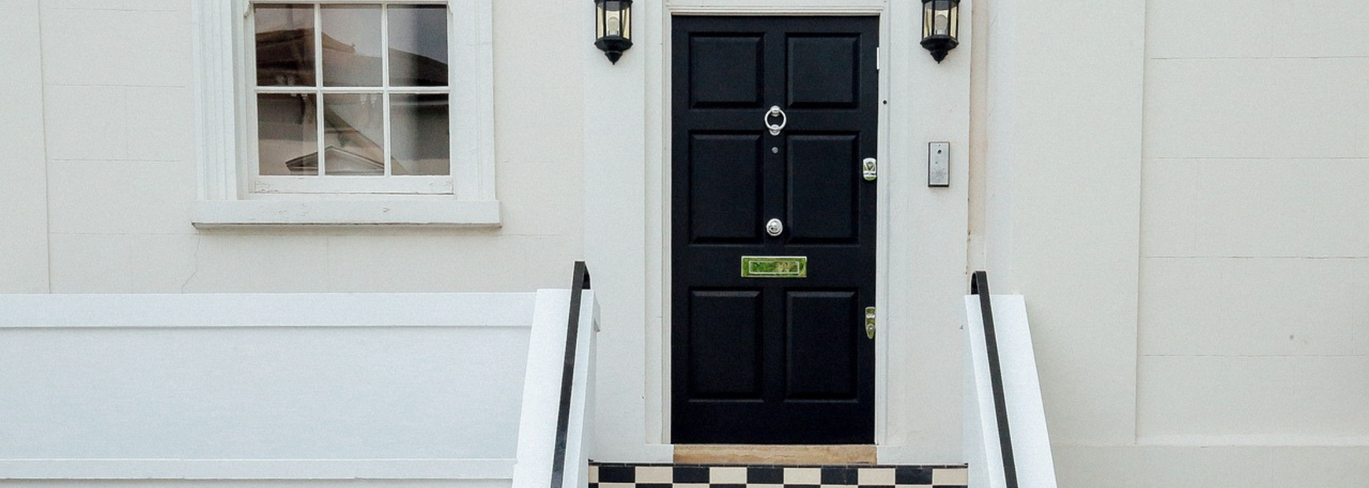 White building facade with a black front door, window, and steps with railings