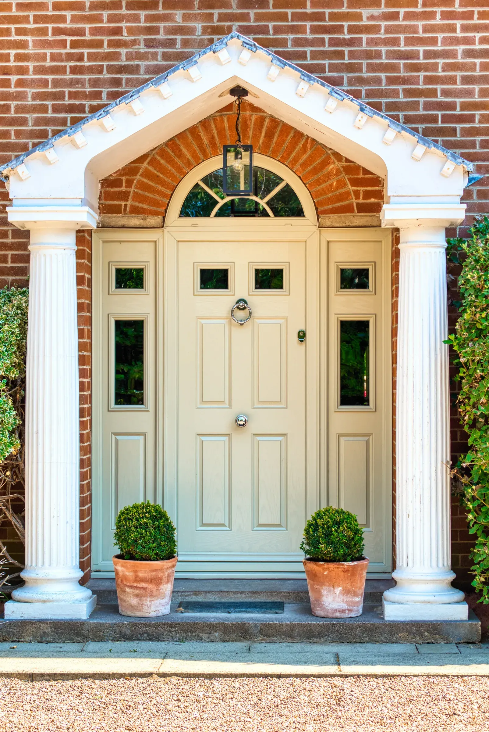 Front entrance with cream double doors, white columns, and potted plants against a brick facade.