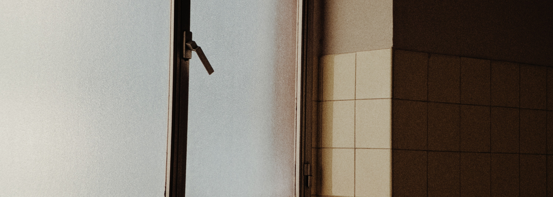 Open doorway with a glass panel and beige tiled wall in soft indoor light
