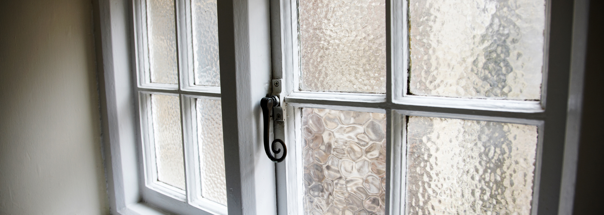 White-painted window with frosted, textured glass and a black latch handle.