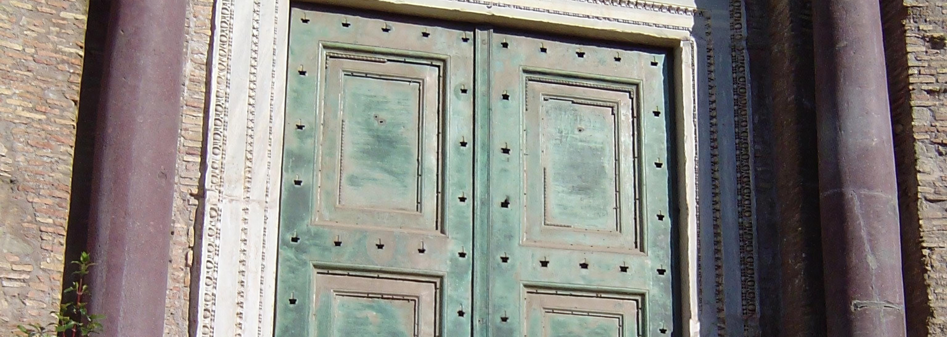 Weathered green double doors framed by ornate stonework and dark columns