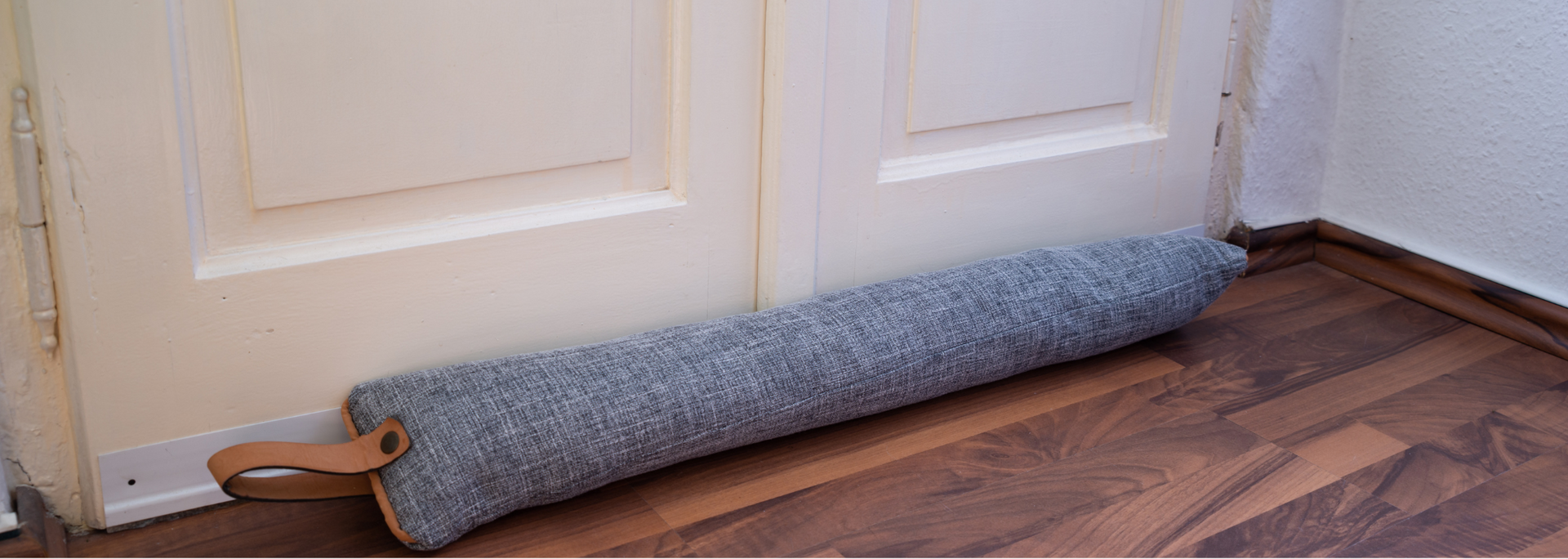 Gray draft stopper rolled along the bottom of a white door on a wood floor
