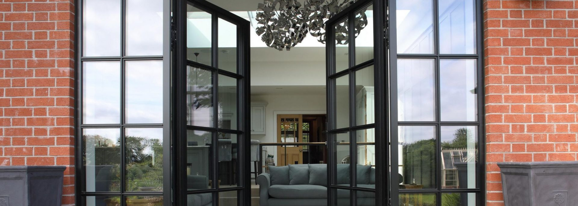 Open black French doors framing a bright living room with gray sofa and red brick walls