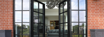 Open black French doors framing a bright living room with gray sofa and red brick walls