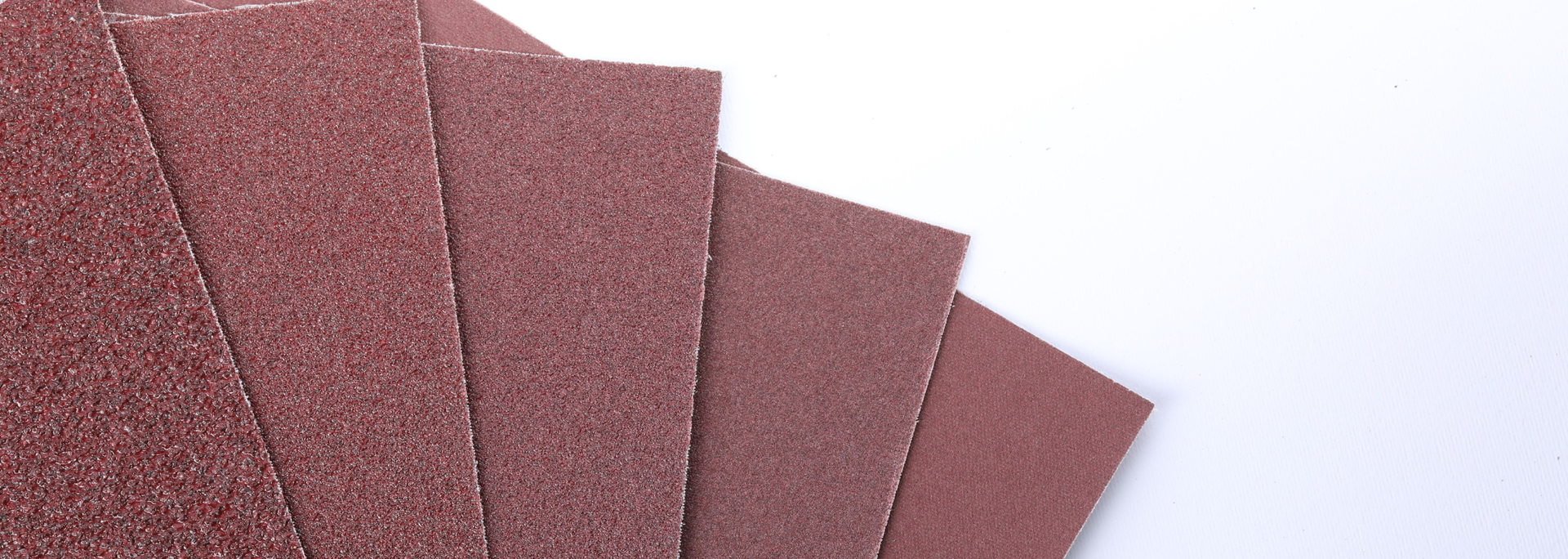 Stacked maroon sanding sheets fanned out on a white surface.