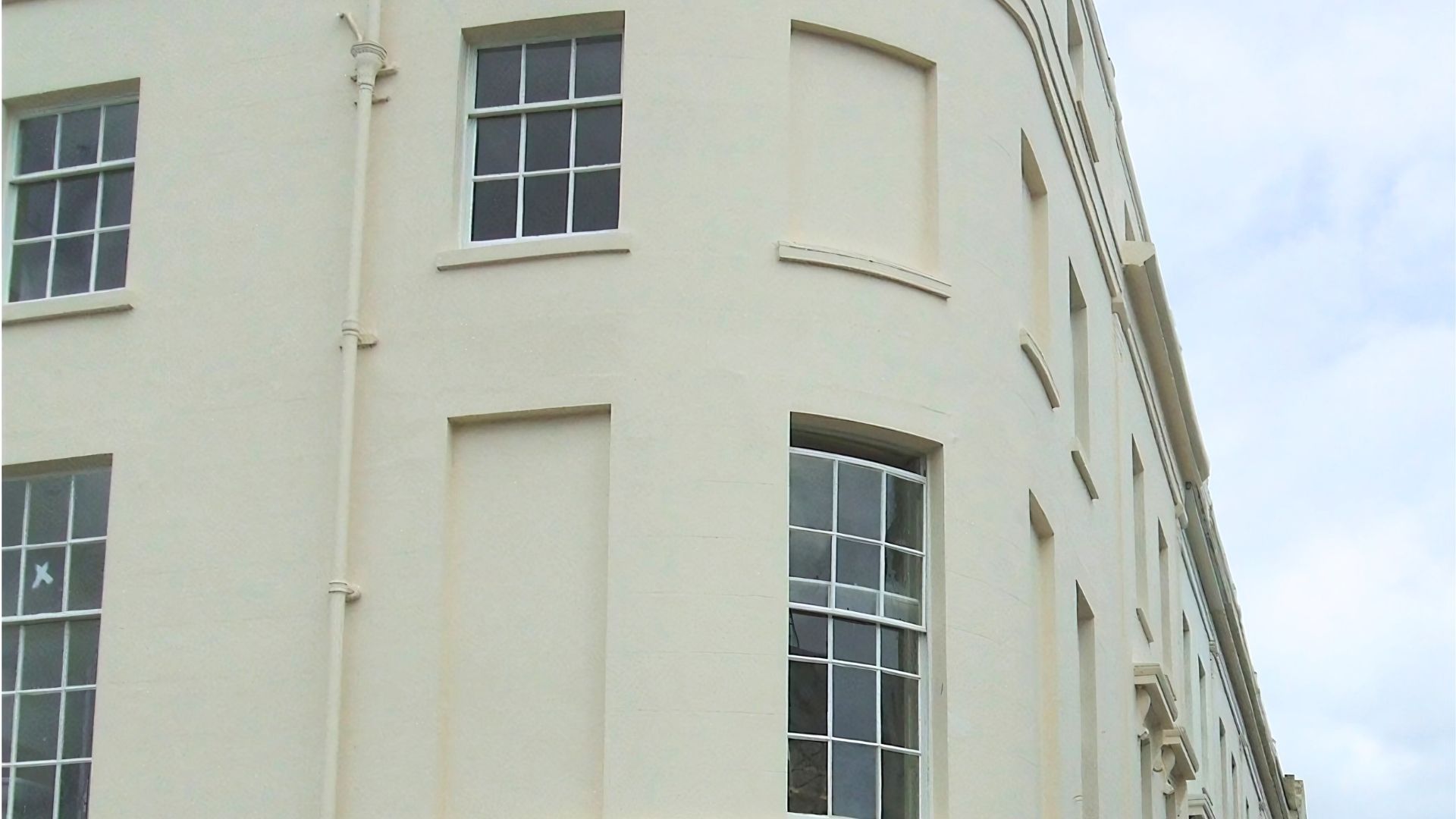 Corner of a cream-colored building with tall windows and a pale sky in the background