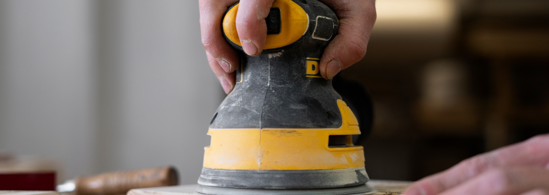 Hand sanding a wooden surface with a yellow-and-black palm sander