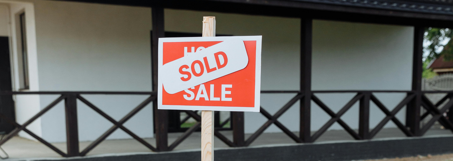 For Sale sign with a red SOLD sticker on a porch railing