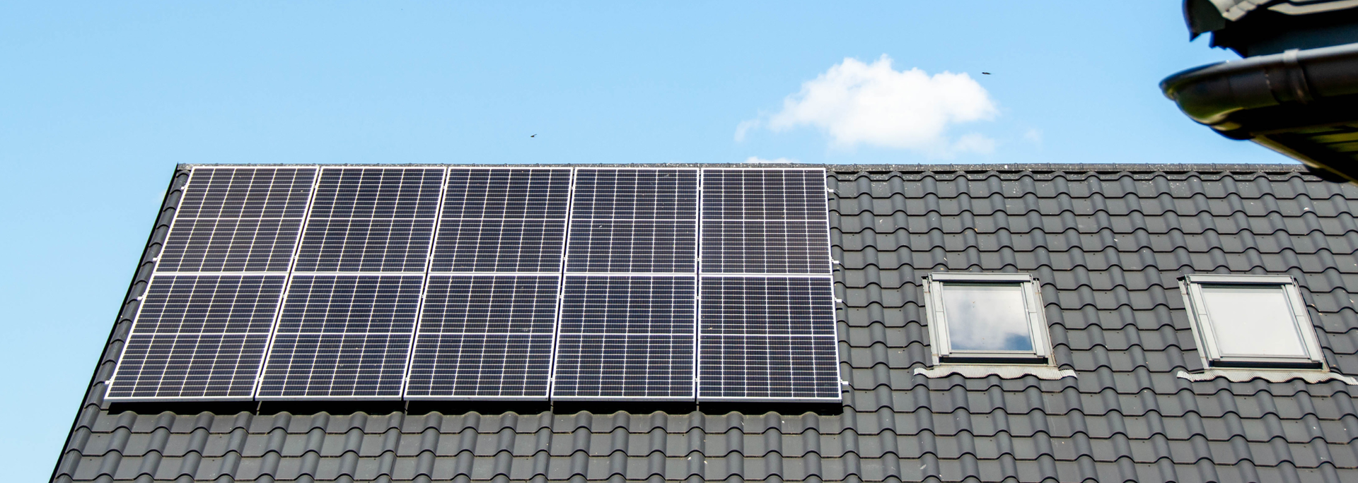 Solar panels mounted on a dark shingle roof beneath a blue sky